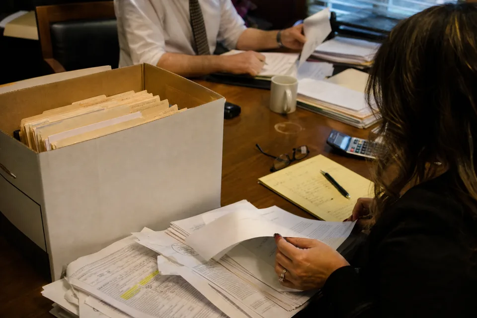 Box of tabbed medical records, a highlighted hospital bill and a calculator on a law firm conference table